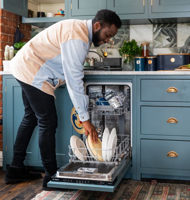 Young black male homeowner loading their dishwasher in the kitchen